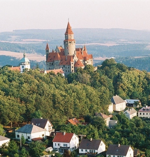 Panoramatický pohled na hrad Bouzov, který se tyčí nad hustým lesem.